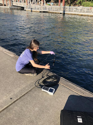 student holding scientific equipment near river