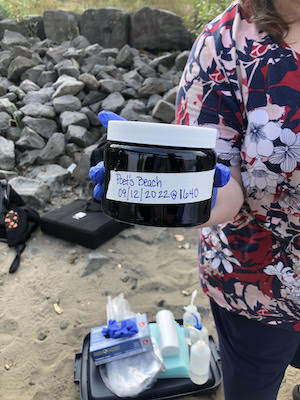 hand holding black jar with white lid labeled "Poets Beach"