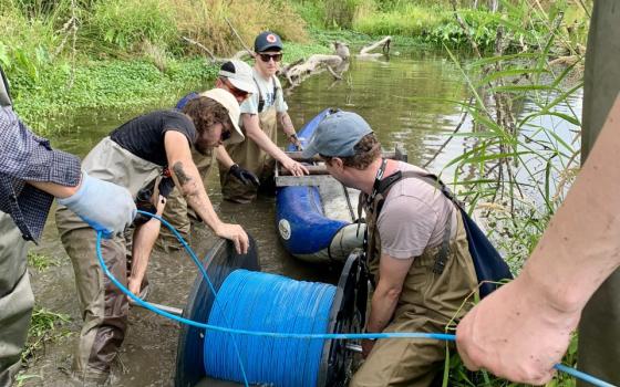Researchers are setting up water temperature equipment, a long blue cable, in a stream