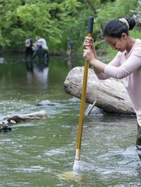 A woman stands in a river measuring the depth of the water
