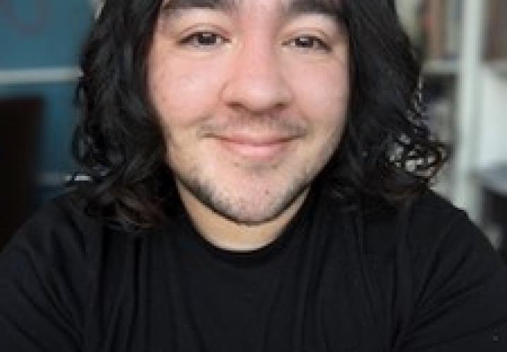 Student with medium-length dark curly hair and a black shirt faces camera smiling