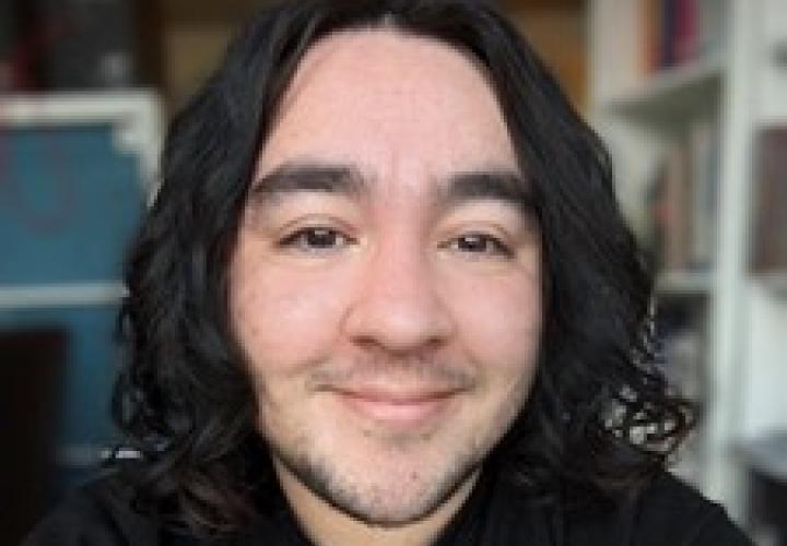 Student with medium-length dark curly hair and a black shirt faces camera smiling