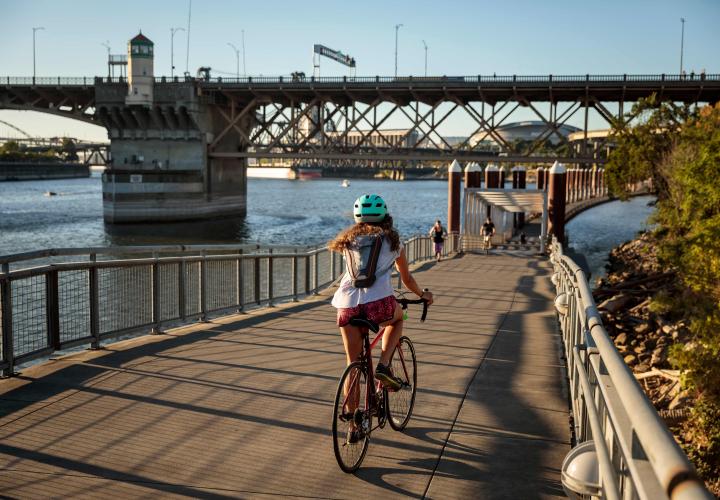 Woman on a bike riding down a pedestrian and bike path next to the Willamette River