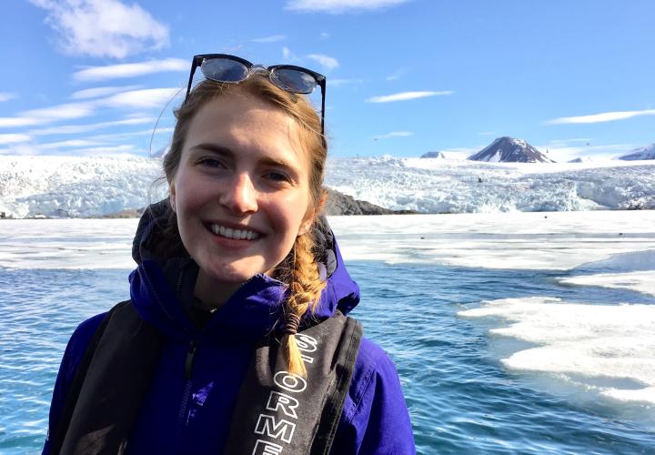 woman with sunglasses on her head in front of deep blue water and a glacier