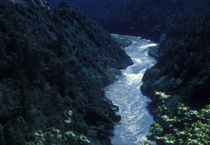 The Klamath River flows in a canyon below steep rocky and forested slopes.