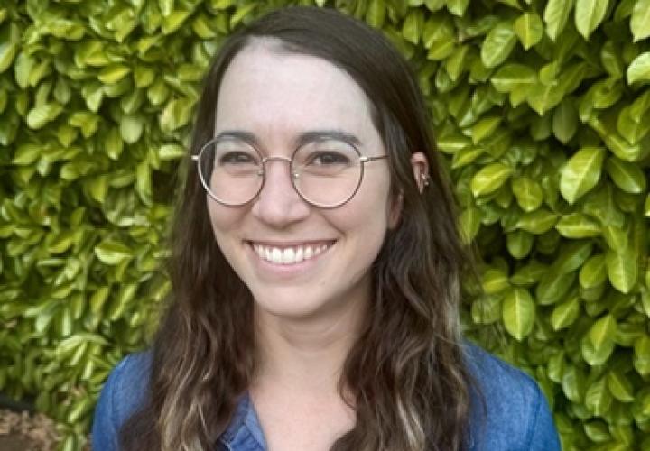 Young Caucasian woman with round glasses and long brown hair who is smiling.