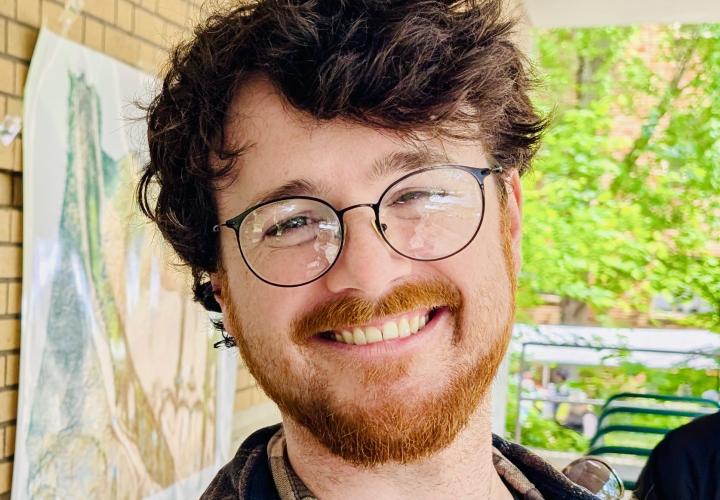 A smiling man with brown hair, a beard, and glasses 