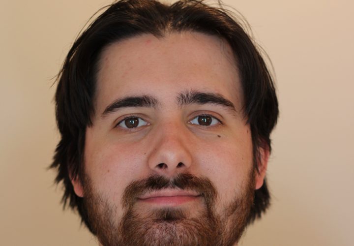 A man with brown hair and a beard against a beige background