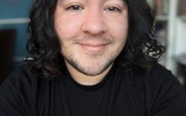 Student with medium-length dark curly hair and a black shirt faces camera smiling