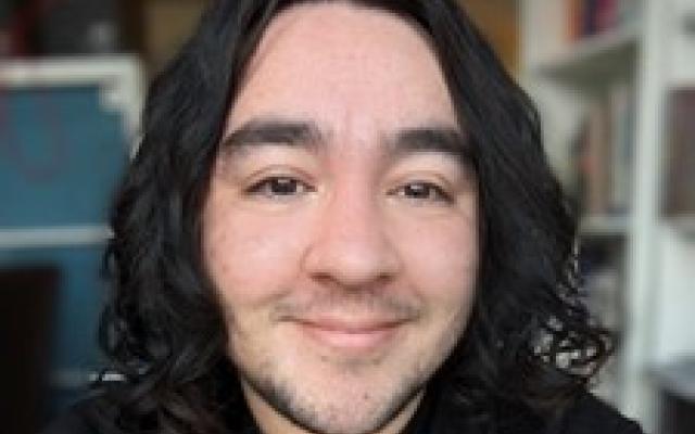 Student with medium-length dark curly hair and a black shirt faces camera smiling