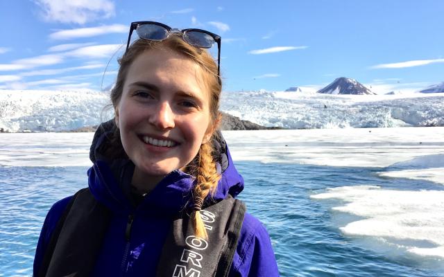 woman with sunglasses on her head in front of deep blue water and a glacier