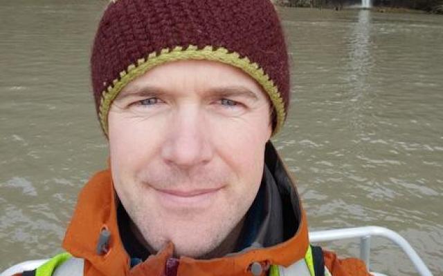 Headshot of Will Long, wearing a maroon beanie, orange rainjacket and reflective safety vest.