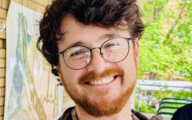A smiling man with brown hair, a beard, and glasses 