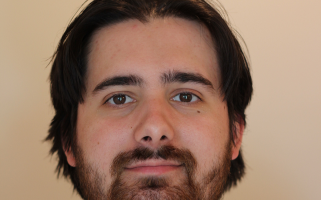 A man with brown hair and a beard against a beige background
