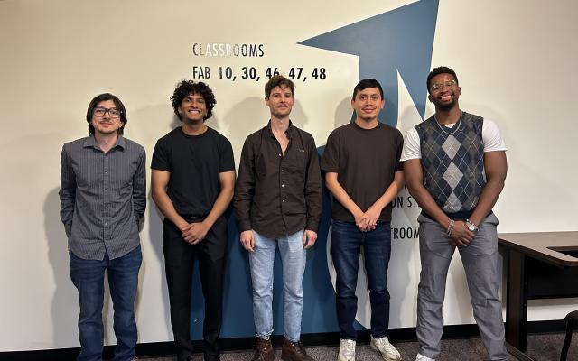 Five students stand together against a wall.