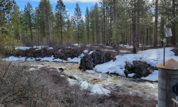 Photo of a flowing river surrounded by ice, rocks, and trees
