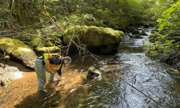 USGS hydrologic technician uses a tool to measure streambed particles in a river.