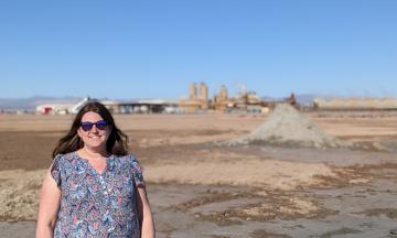 Alida Cantor, a woman with long brown hair, standing in front of hills of mud in the Salton Sea, Imperial Valley area in California