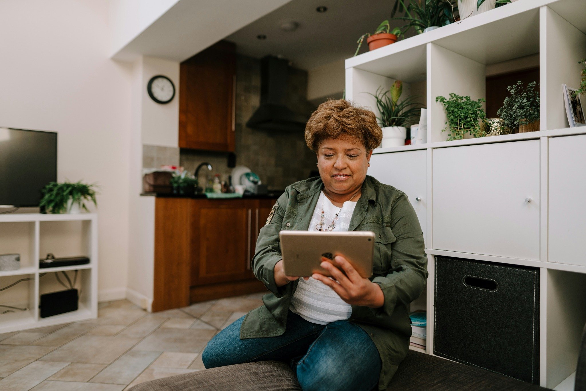 Woman with brown hair and green jacket holds an iPad while sitting on her couch