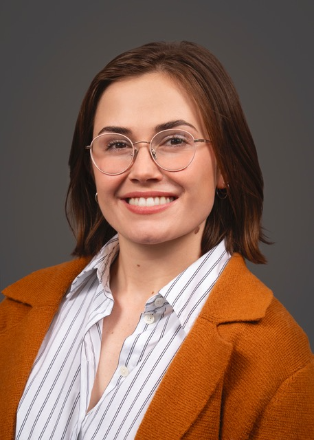 Susan Avila smiles with short brown hair to shoulders, thin-rimmed circular glasses, and orange blazer over a striped blue and white top.