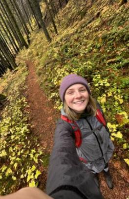 femme person in winter hat hiking on a trail with foliage and trees