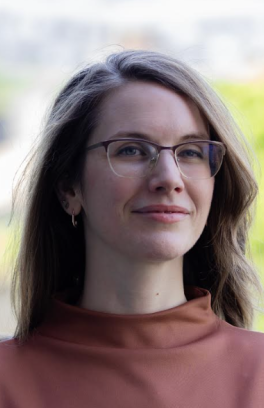 Jeanette smiles at the camera, wearing glasses and a rust colored top.