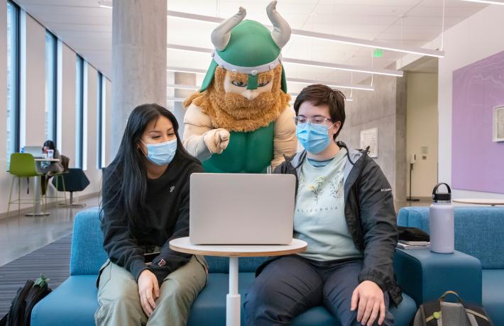 Victor Viking points to computer screen while two students listen.