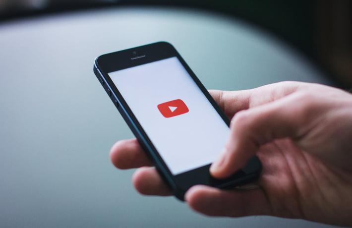A hand holding a cell phone. The YouTube app is showing. 