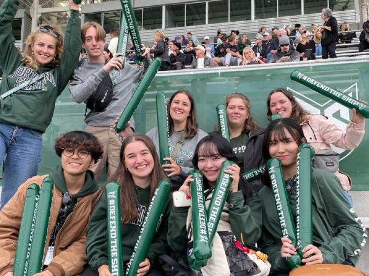 Nine students at a sports event looking at the camera for a group photo.
