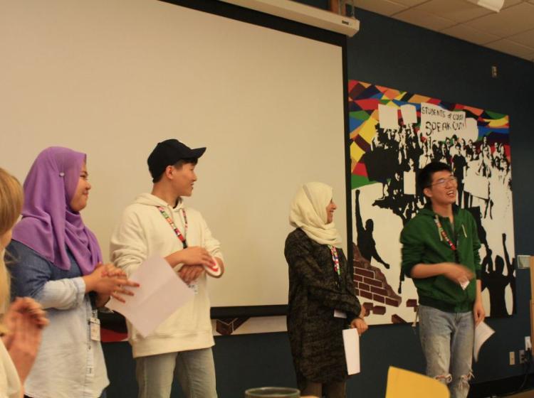 Four student stand at the front of the classroom presenting together.