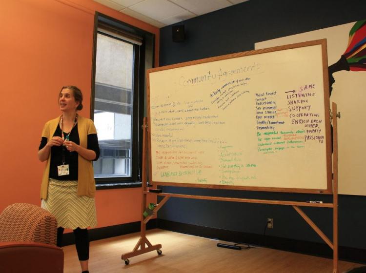 Woman stands in front of white board leading a training.