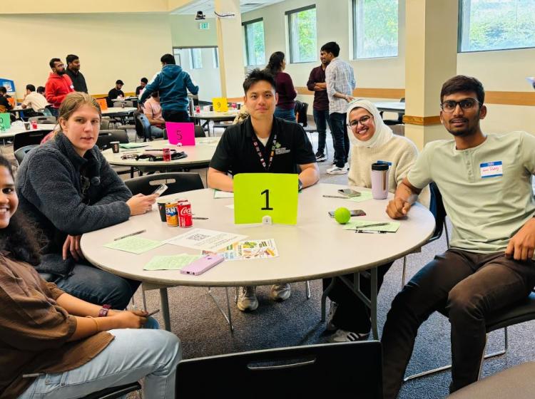 Group of students sit at a round table posing for photo.