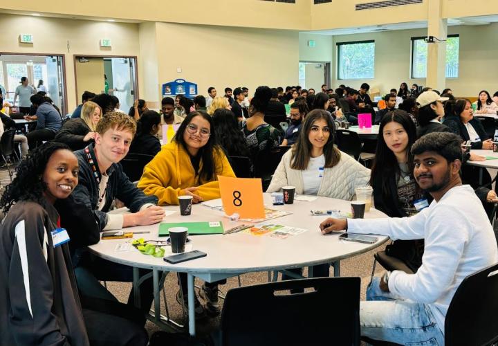 Group of students sit at a round table smiling at the camera.