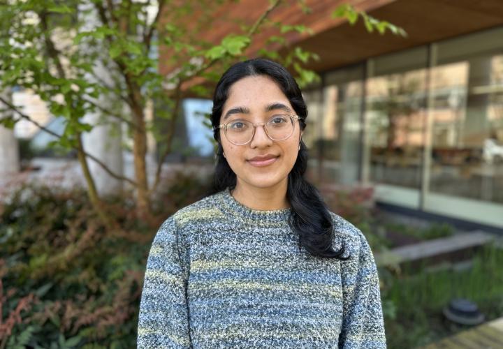 Female student poses for a headshot outside with greenery in the background.