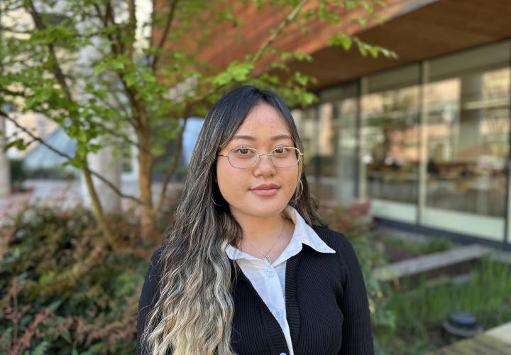 Female student poses for a headshot outside with greenery in the background.