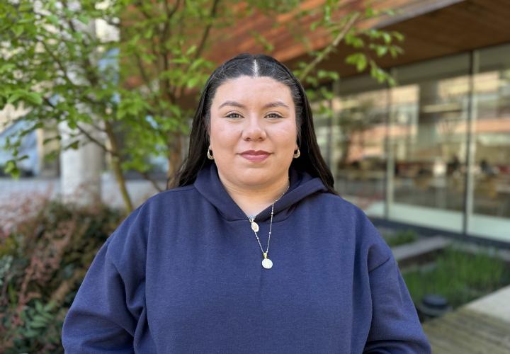 Female student poses for a headshot outside with greenery in the background.