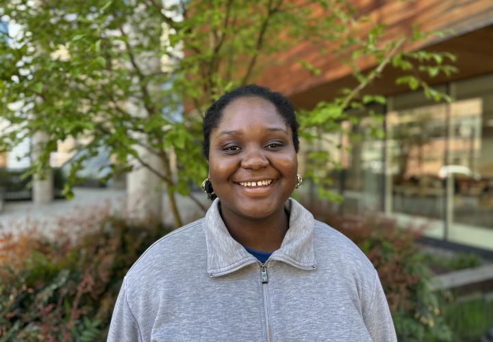 Female student poses for a headshot outside with greenery in the background.