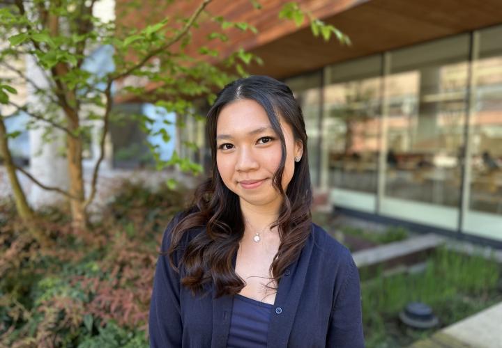 Female student poses for a headshot outside with greenery in the background.