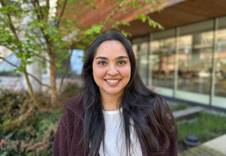Female student poses for a headshot outside with greenery in the background.