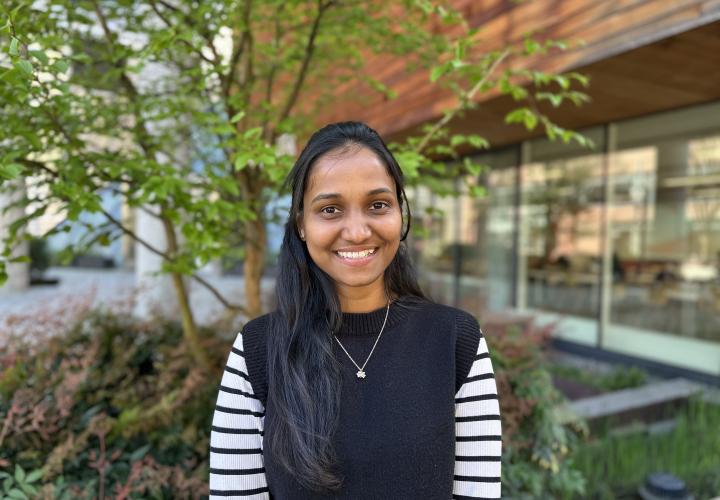 Female student poses for a headshot outside with greenery in the background.