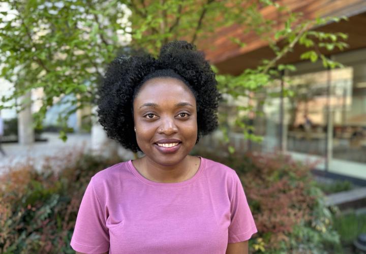 Female student poses for a headshot outside with greenery in the background.