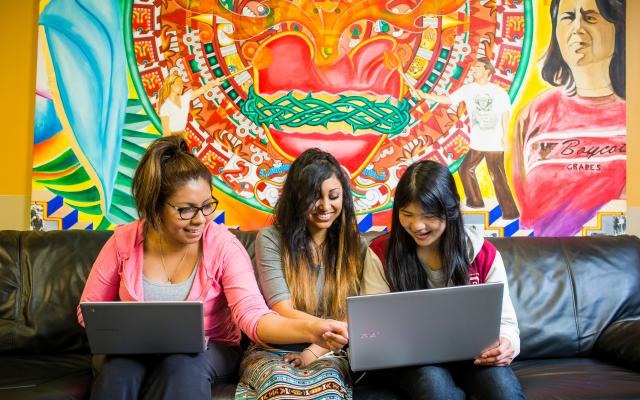 Three girls sitting on sofa looking at personal computers.