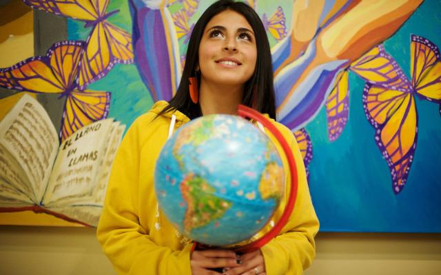 Student poses at the camera holds world globe.