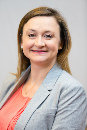 A professional photo of Dr. Kahn in a grey blazer and coral blouse on a white background.