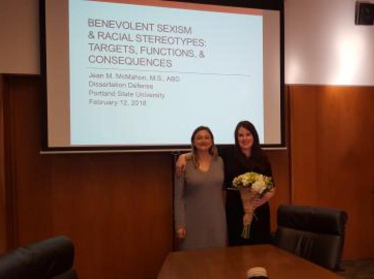 Dr. Kahn and Jean McMahon standing in front of the projected presentation slides for Jean's dissertation defense meeting. The slide reads: "Benevolent Sexism and Racial Stereotypes: Targets, Functions, and Consequences. Jean M. McMahon Dissertation Defense. Portland State University, February 12th, 2018.