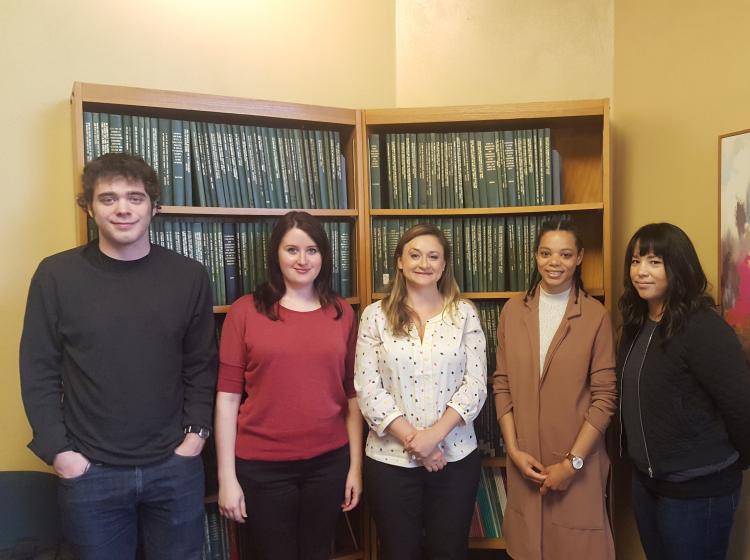 Photo of GRASP lab members in 2017. Dr. Kahn stands with two graduate students and two undergraduate research assistants in front of a bookshelf, a multi-colored abstract painting, and yellow walls.