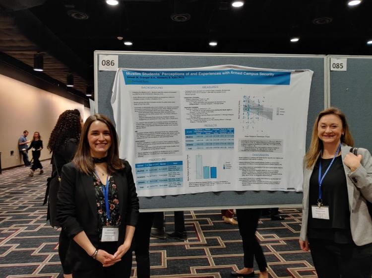 Dr. Kahn and Aeleah Granger standing in front of Aeleah's poster at the SPSP 2020 annual conference. The poster is titled: "Muslim Students Perceptions of and Experiences with Armed Campus Security".