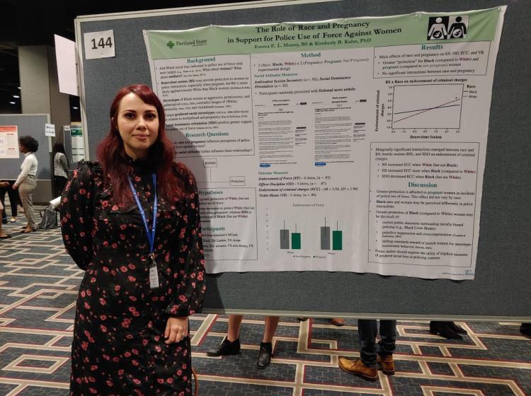 Emma Money standing in front of her poster at SPSP 2020 annual conference. The poster is titled: "The Role of Race and Pregnancy in Support for Police Use of Force Against Women".