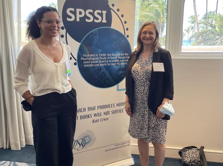 Jaboa Lake and Kimberly Kahn standing together at the 2022 Annual SPSSI Conference in front of a sign with the SPSSI logo.