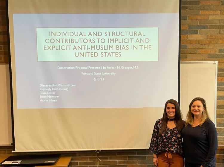 Aeleah Granger and Kimberly Kahn standing in front of Aeleah's title slide for her dissertation proposal in June of 2023. The title reads "Individual and structural contributors to implicit and explicit anti-Muslim bias in the United States"